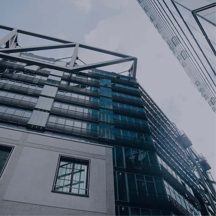 Upward view of modern office buildings with glass windows and metal structural elements under a cloudy sky.
