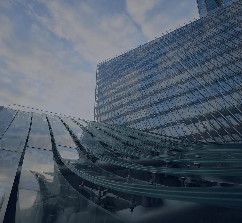Modern glass building with curved glass panels in the foreground reflecting a cloudy sky.