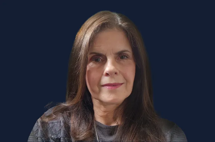 Portrait of a middle-aged woman with long brown hair wearing a gray sweater against a dark blue background.