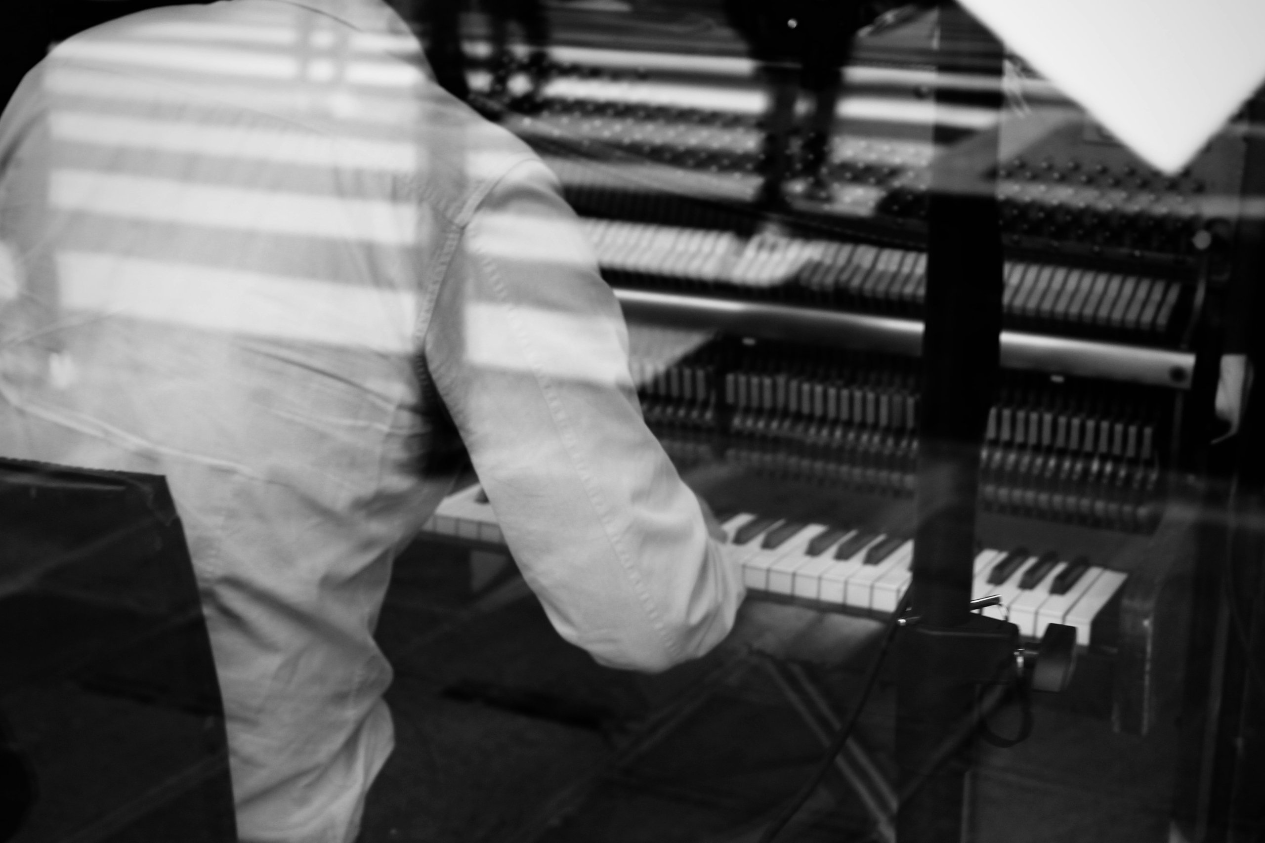 A photo of a man playing the piano behind a window