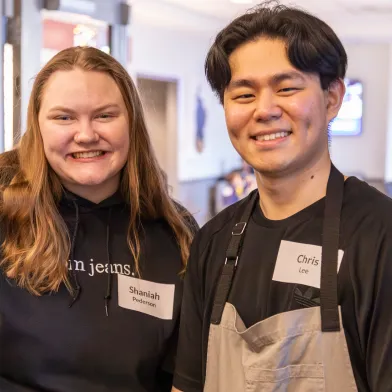 Two smiling coworkers in black shirts and aprons at workplace