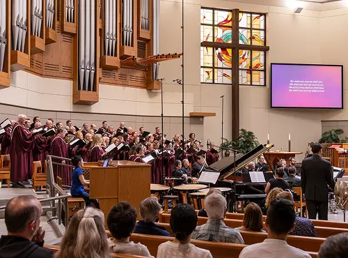 Choir performing in church with organ, piano, and stained glass window