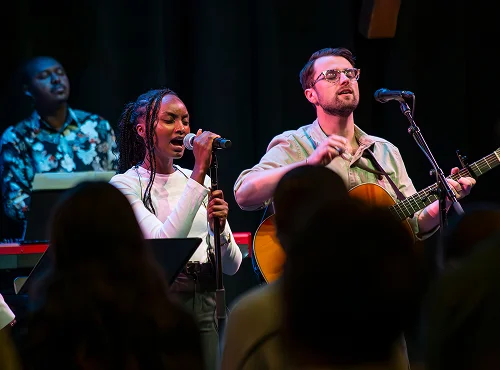 Two musicians performing on stage, singing and playing acoustic guitar