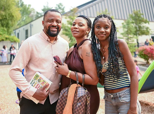 Three people smiling together outdoors, holding bags and posing