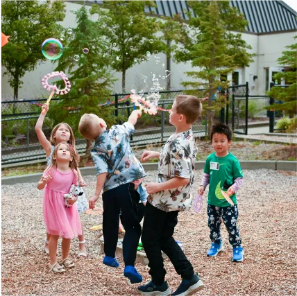 Children playing with bubble wands outdoors on a gravel playground