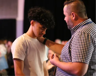 Two people in conversation, one gesturing to the other in a dimly lit space