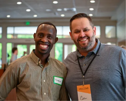 Two smiling colleagues at a conference wearing name tags and welcome lanyards