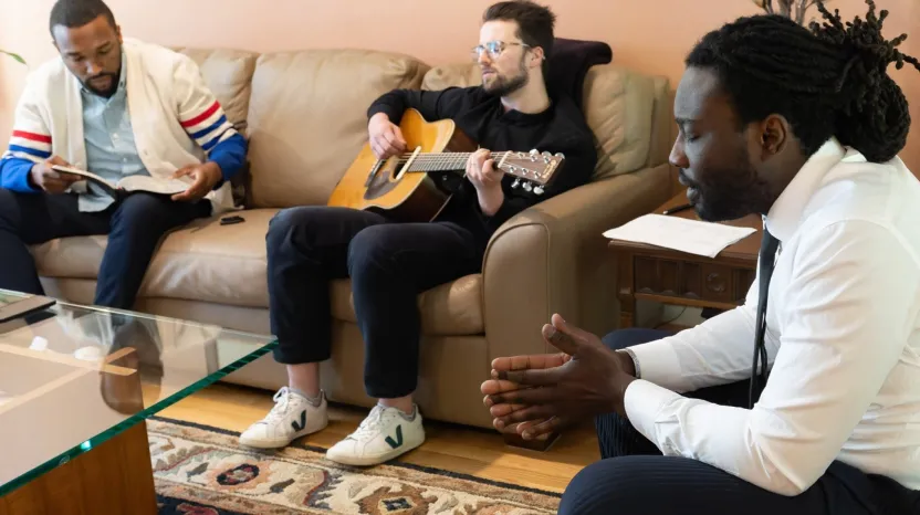 Three men in casual setting, one playing acoustic guitar