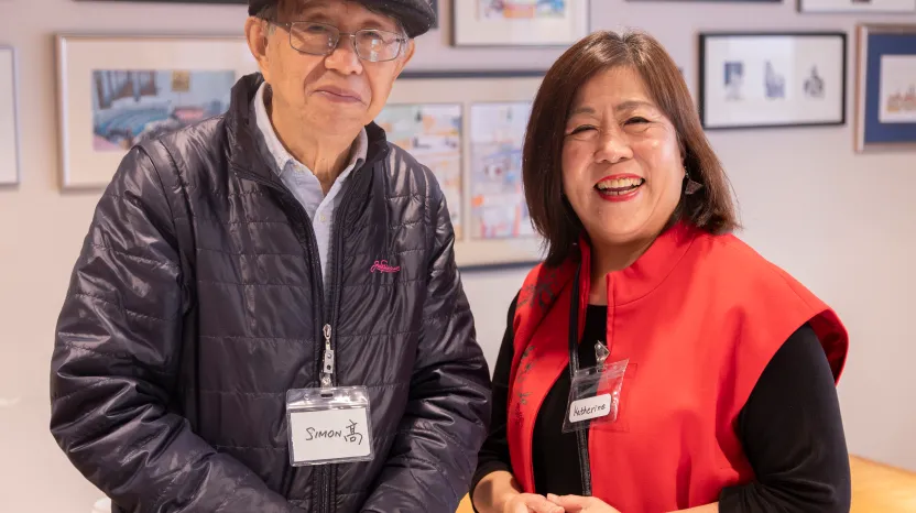 Two seniors with name tags smile in art gallery or community center