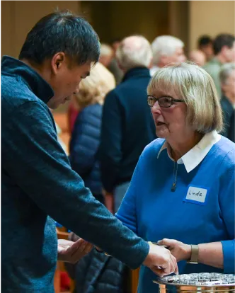 Volunteer in blue sweater shakes hands with attendee at community event