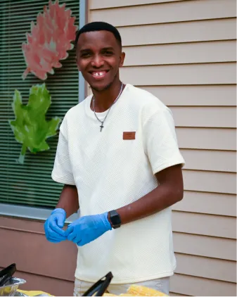Smiling person in white shirt and blue gloves preparing food outdoors