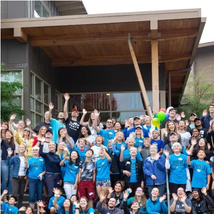 Large group of enthusiastic people in blue shirts cheering together outside building