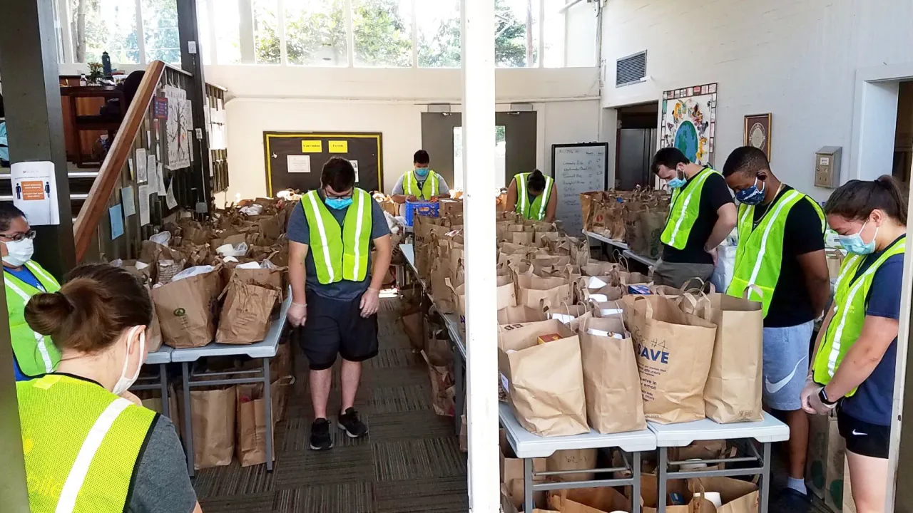 Volunteers in safety vests pack brown paper bags in community space