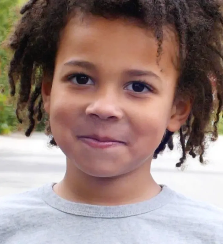 Young child with curly hair smiling softly at the camera