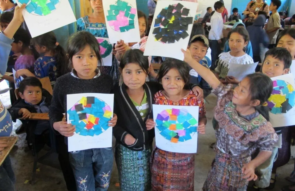 Children holding colorful collage artworks in a classroom setting