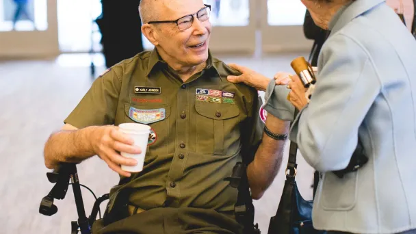 Veteran in military uniform sitting in wheelchair, smiling with coffee cup