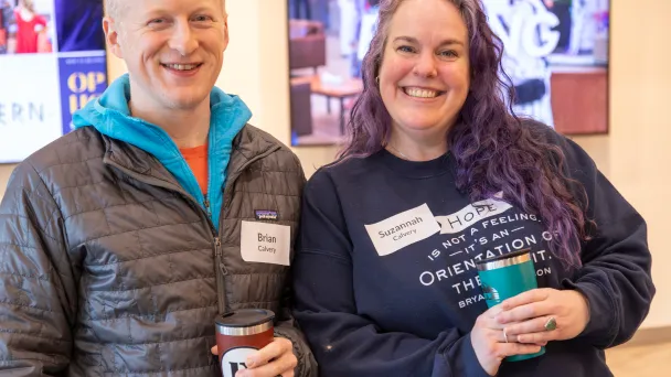 Two smiling conference attendees with name tags holding coffee cups