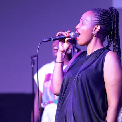 Female singer performing passionately on stage with microphone in purple lighting