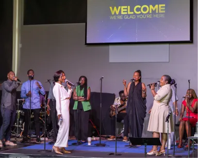Diverse group of singers on stage with welcome screen in background