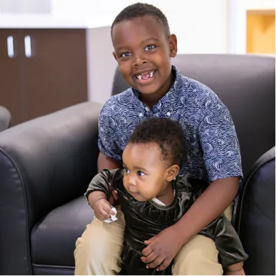 Smiling boy hugging younger child on leather couch