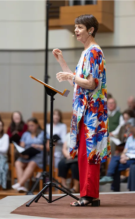 Speaker in colorful floral top gives presentation at podium with audience