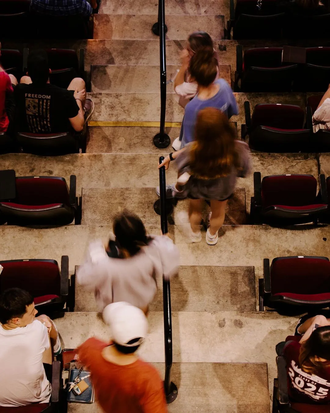 People moving up stone stairs in blurred motion between red seats