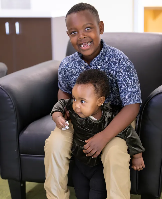 Smiling older child holding younger sibling on black leather chair