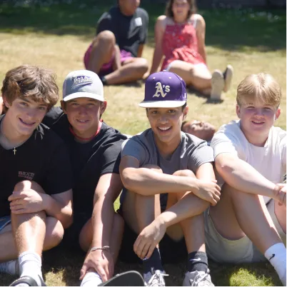 Group of friends sitting together on grass, smiling on a sunny day