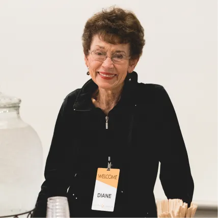 Smiling older woman wearing black jacket with welcome name tag