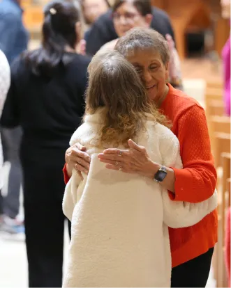 Two women hugging warmly, smiling in a crowded indoor space
