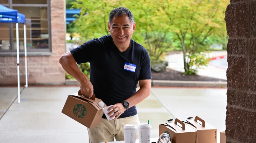 Smiling employee holding Starbucks coffee box outdoors near building