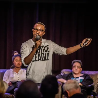 Speaker on stage with microphone, gesturing during panel discussion
