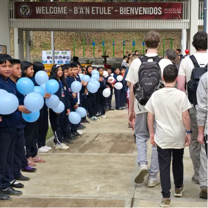 Students with blue balloons gather under 'Welcome' sign at school event