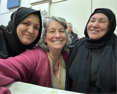 Three smiling women, two in hijabs, posing together warmly