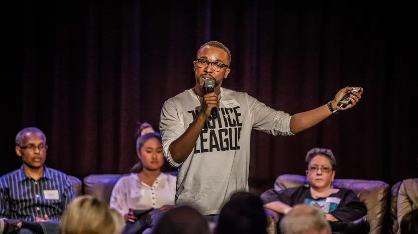 Speaker in glasses gestures while talking into microphone on stage