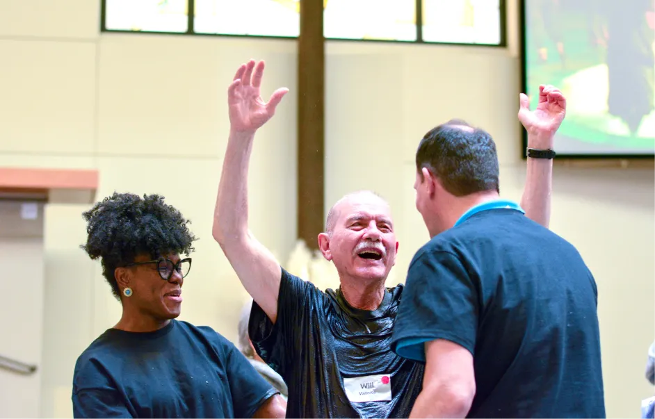 Excited older man with raised hands laughing with colleagues in meeting