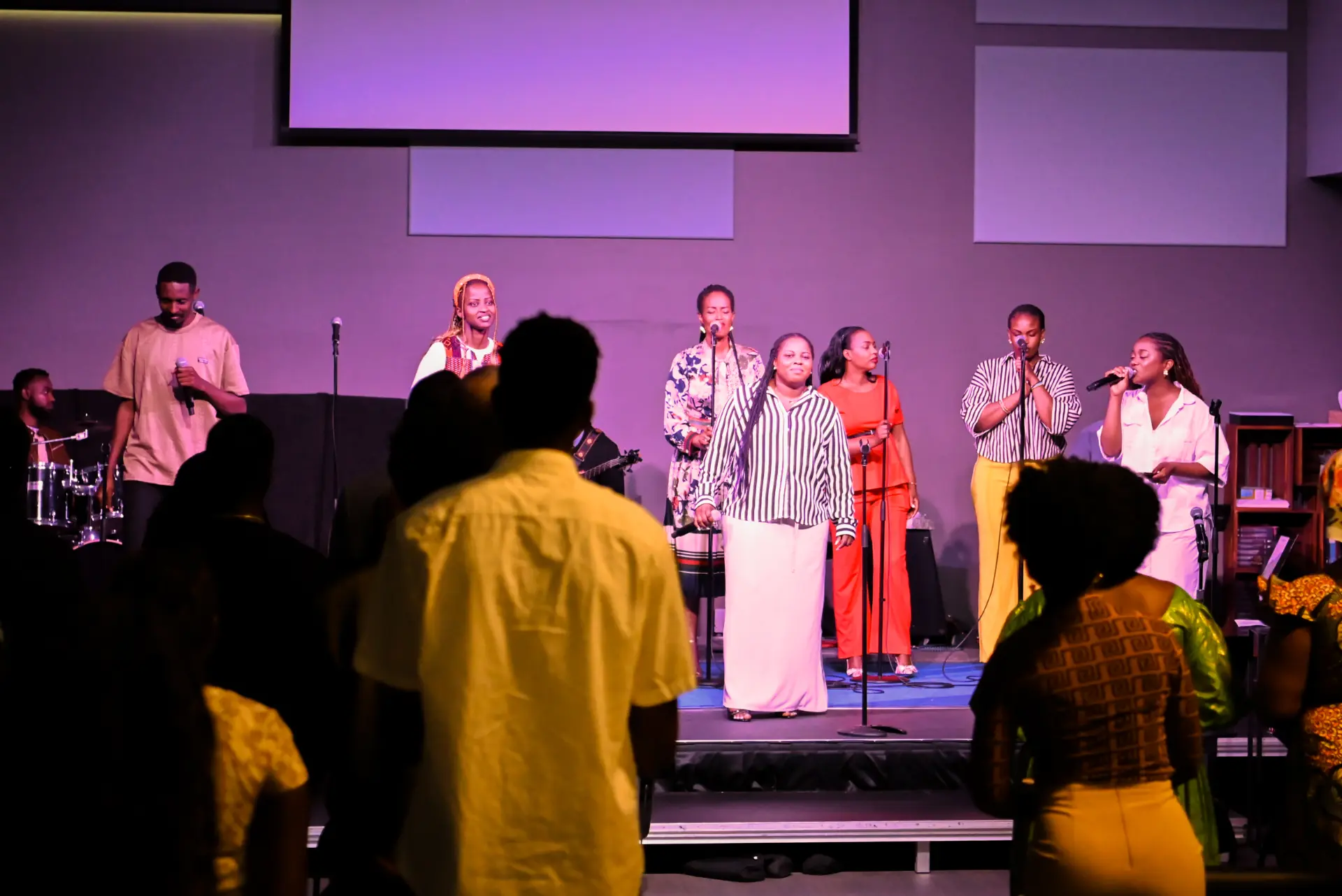 A worship team sings and plays music on stage while the congregation stands and participates during a church service.