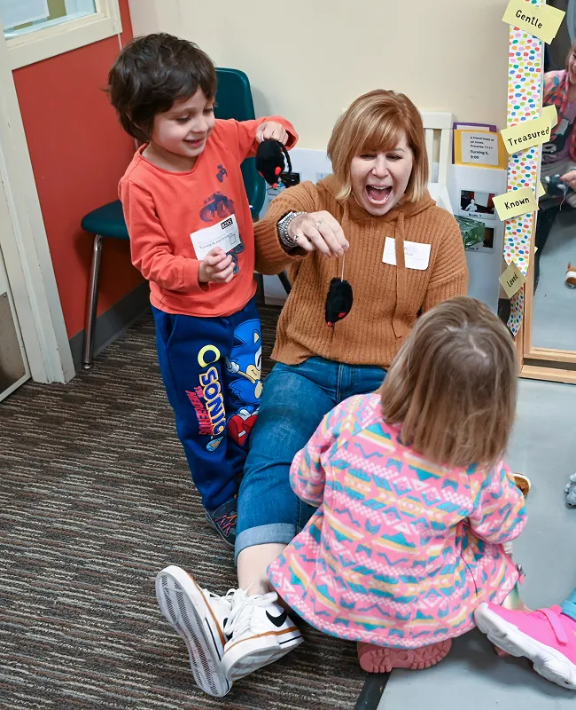 Teacher and children playing and laughing together in colorful classroom
