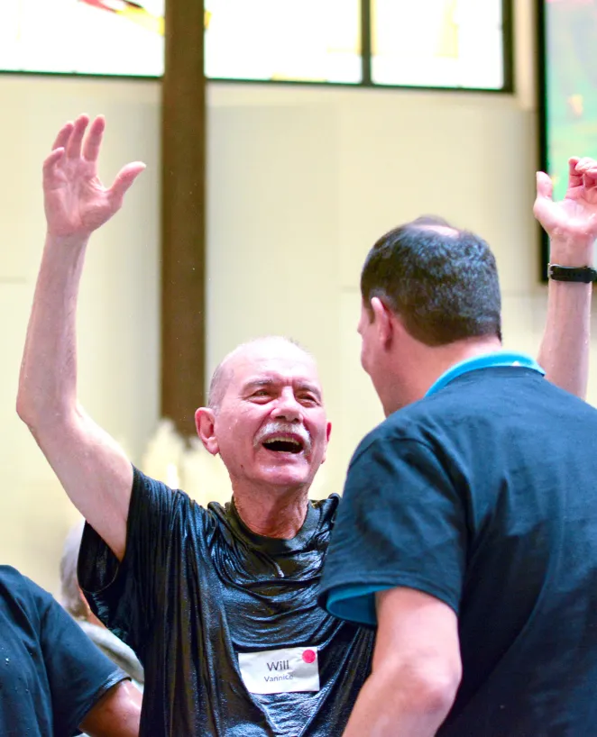 Older man laughing and raising hands during an energetic group activity