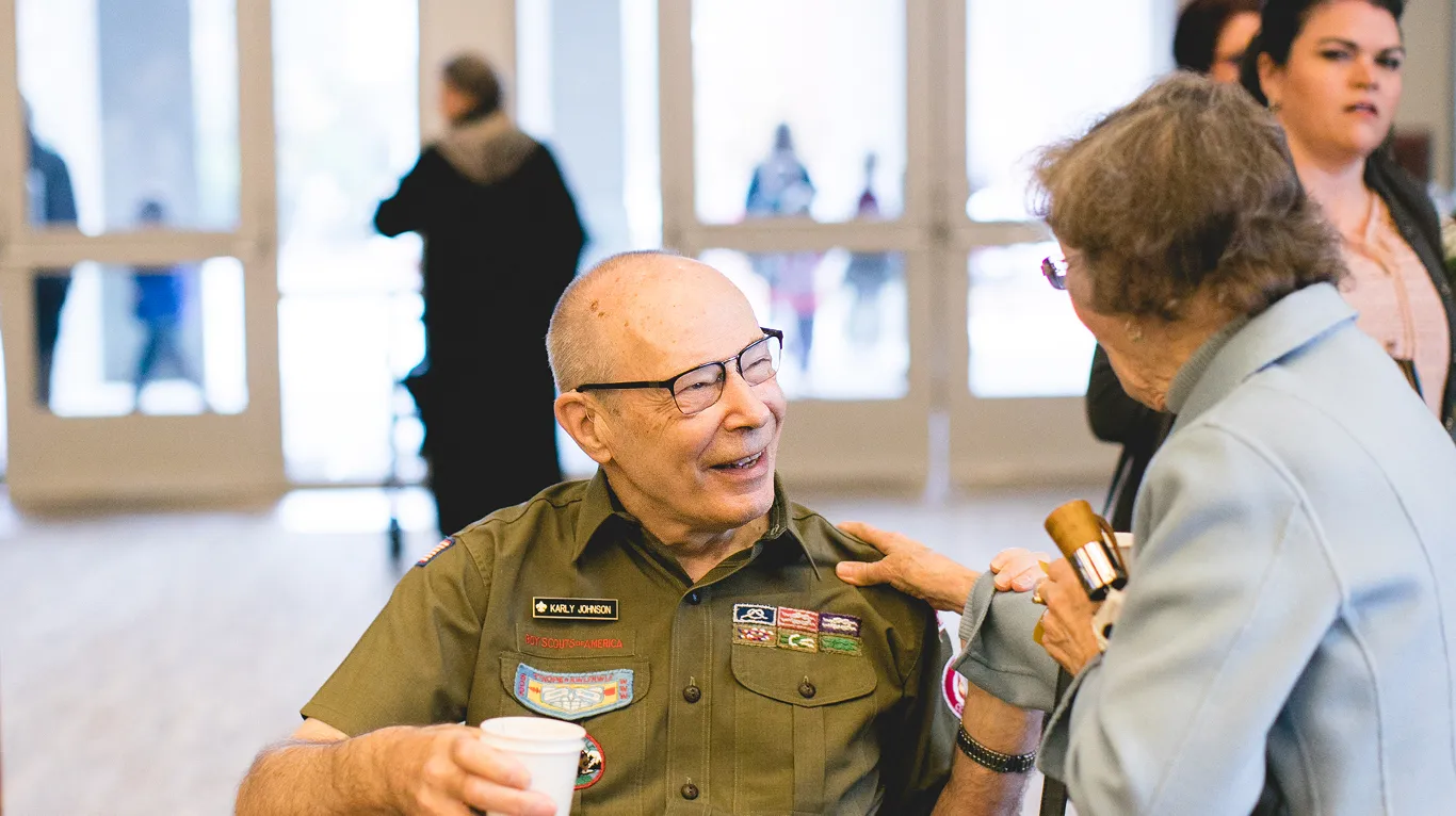 Smiling scout leader in uniform chatting with colleague, holding coffee