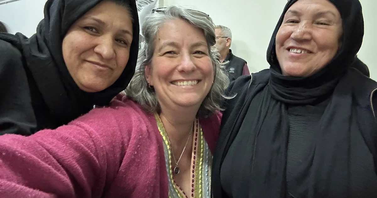 Three women smiling together, two wearing black hijabs