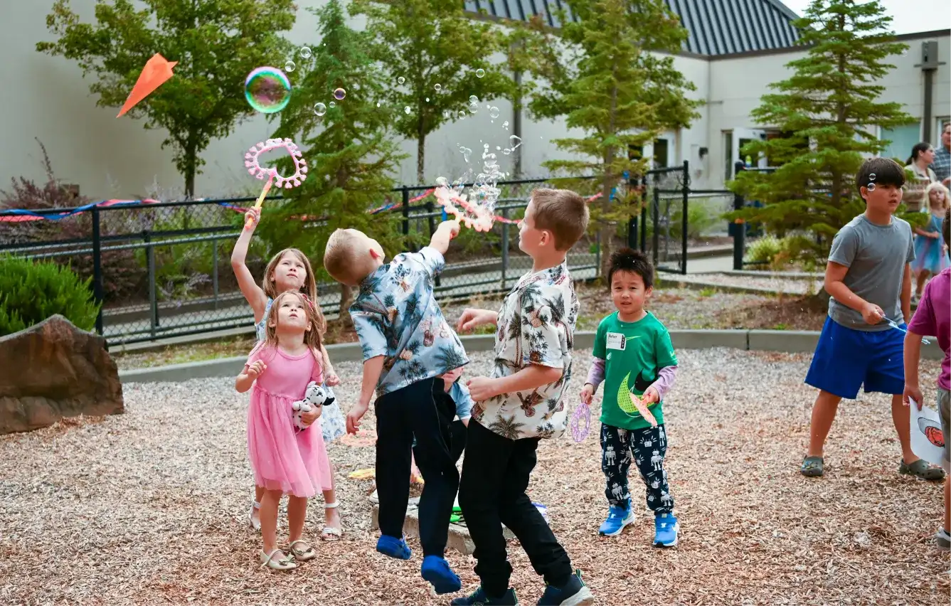Children playing with colorful bubble wands in an outdoor courtyard