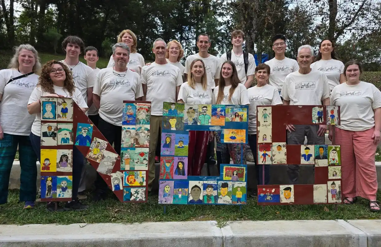 Group with white shirts posing with colorful portrait art panels outdoors