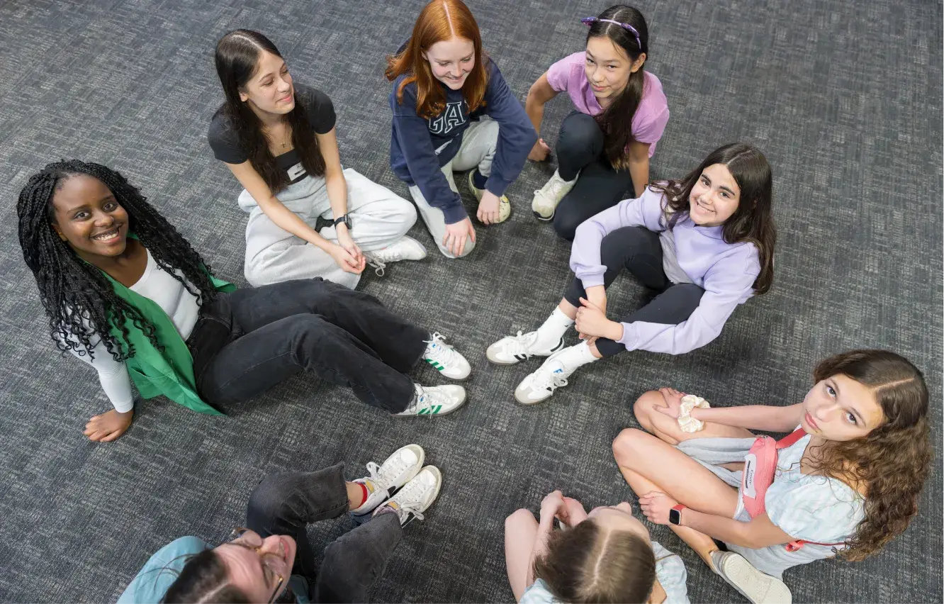 Group of diverse students sitting in circle on carpet, smiling together