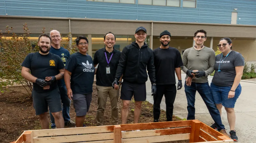 Diverse group of people posing together near wooden planter outside building