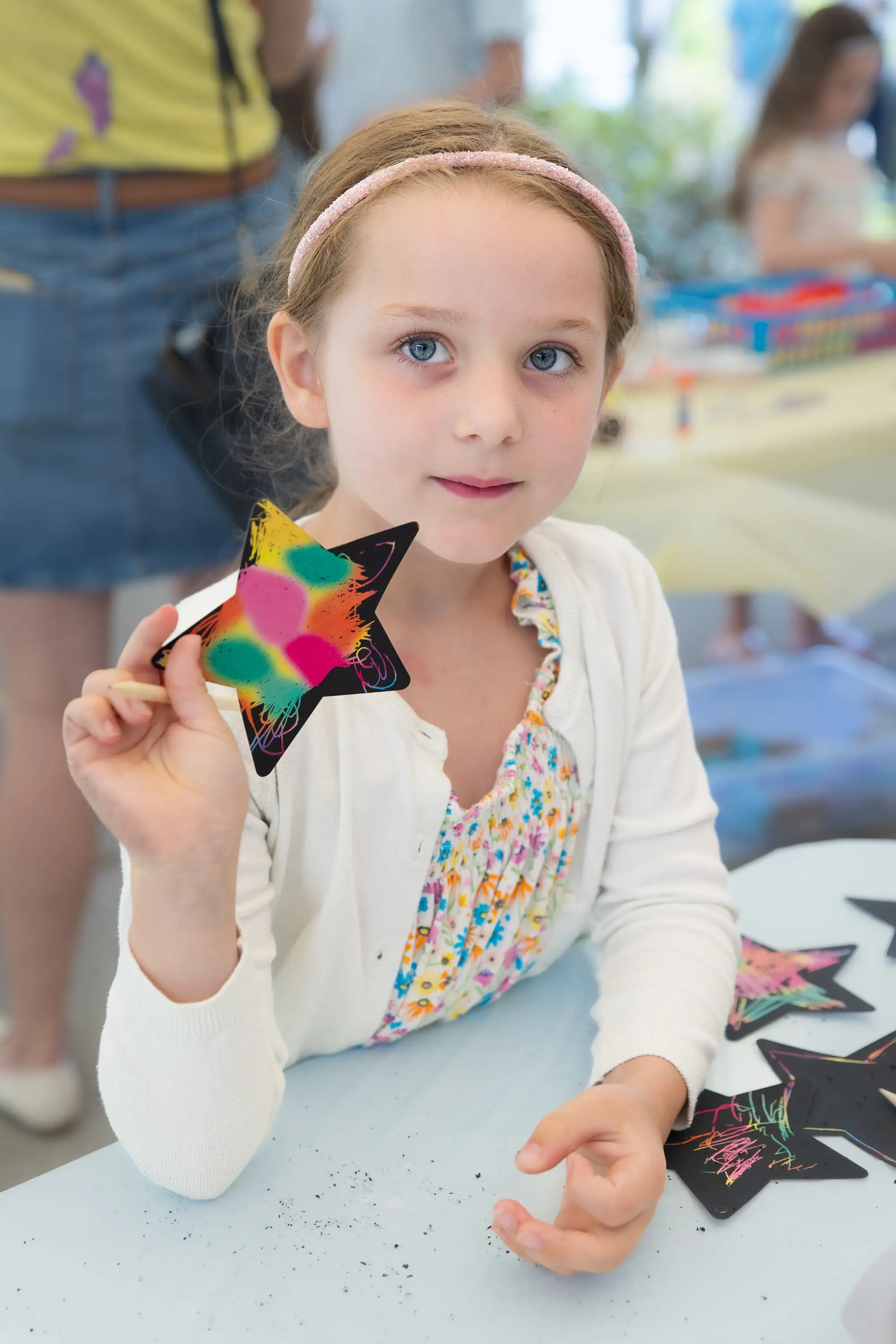 Young girl holding a colorful star-shaped craft during an arts and crafts activity at a community event.
