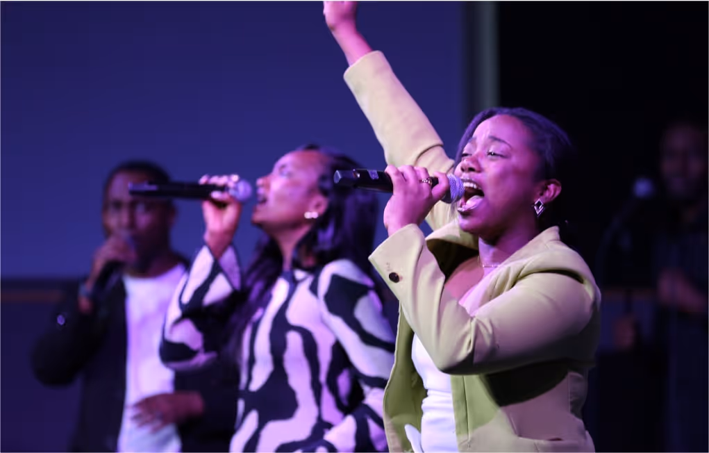 Three people singing passionately into microphones, with the woman in front raising one arm.