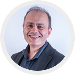Smiling middle-aged man with short gray hair wearing a dark blazer and shirt against a light background.
