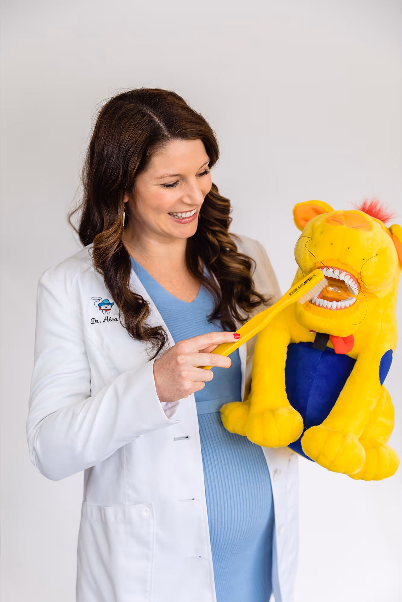 A pregnant woman in a white lab coat holding a yellow stuffed animal.