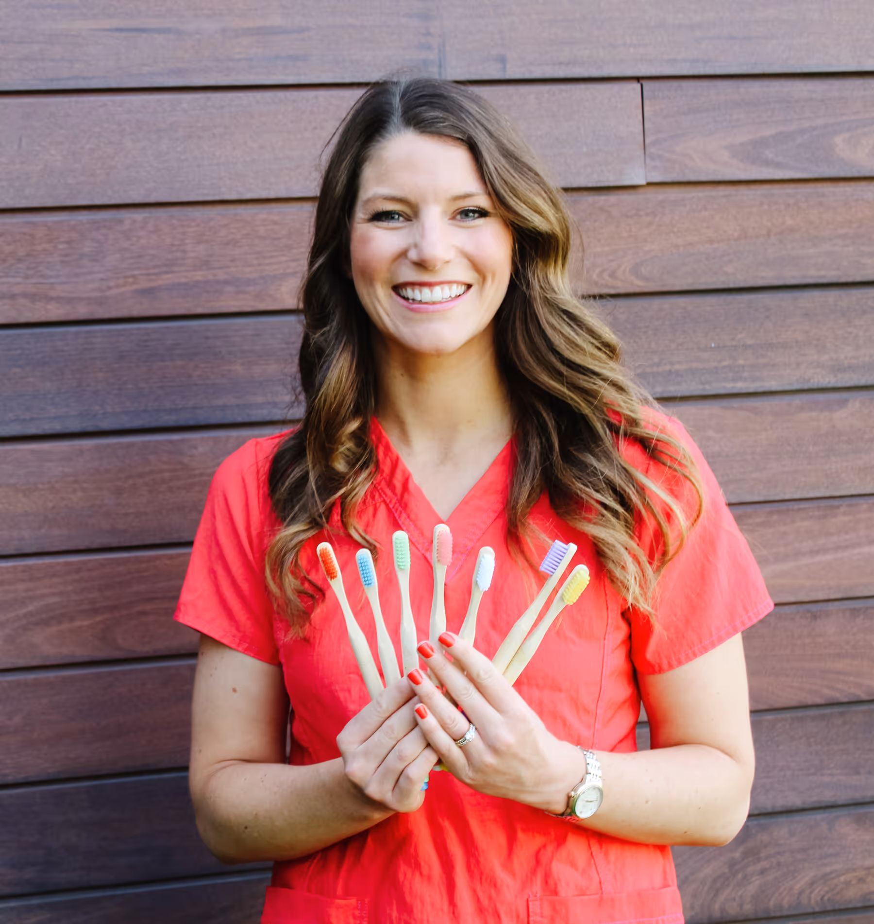 A woman in a red shirt holding a bunch of toothbrushes.